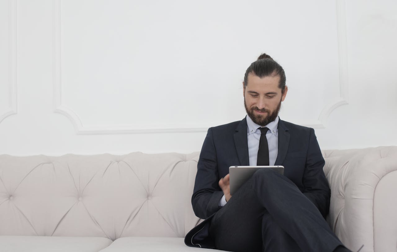 services-03 A businessman in a suit sitting on a sofa using a tablet, smiling.